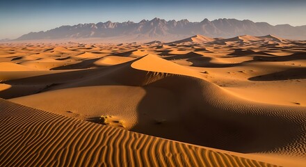 Golden desert dunes stretch towards majestic mountains under a clear blue sky.