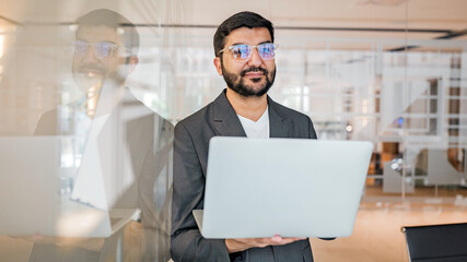 Man using laptop in office setting with glass walls