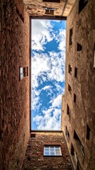 Upward view of aged brick buildings reveals sky with clouds. Architecture surrounds open space with blue sky