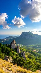 Verdant hills cascade towards distant sea, topped by rocky peaks under a sunny sky dotted with puffy white clouds