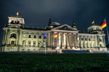 Reichstag building illuminated at night with German flags and dramatic sky in Berlin