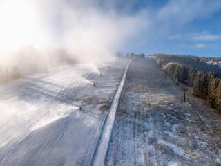 Snowmaking on ski slope with multiple snow cannons preparing pistes in winter mountain resort