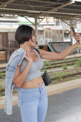 Young woman taking a selfie on a train platform, wearing a light blue outfit with a denim jacket...