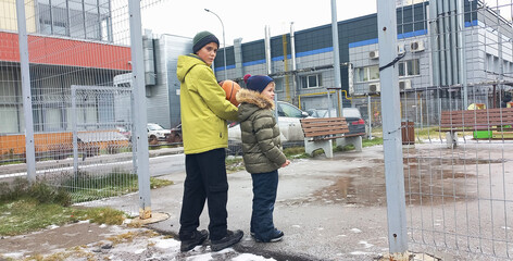 Two boys are standing by a fence in winter, one of them is holding a basketball.