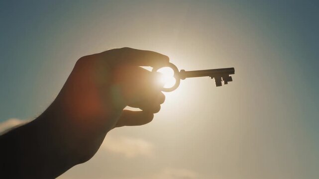Silhouette of a Hand Holding a Key Against a Bright Sunny Sky, Symbolizing Freedom and Hope