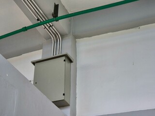 Electrical junction box with exposed conduit pipes mounted on white interior wall ceiling