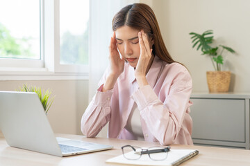 Stressed, exhausted asian young woman having migraine symptoms headache, bored sitting work long time, suffering from dizziness, holding head with hand office syndrome. Health care problem of worker.