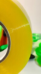 A large roll of yellow transparent shipping tape positioned in front of a utility knife and plastic office supplies for packaging and moving