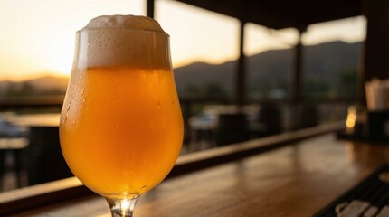 A chilled glass of pale ale with frothy white head rests on a wooden bar overlooking a sunset.