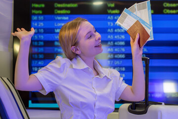Traveler at the airport with passport and boarding passes, rejoicing next to their luggage in front of the flight information board. Happy travel.