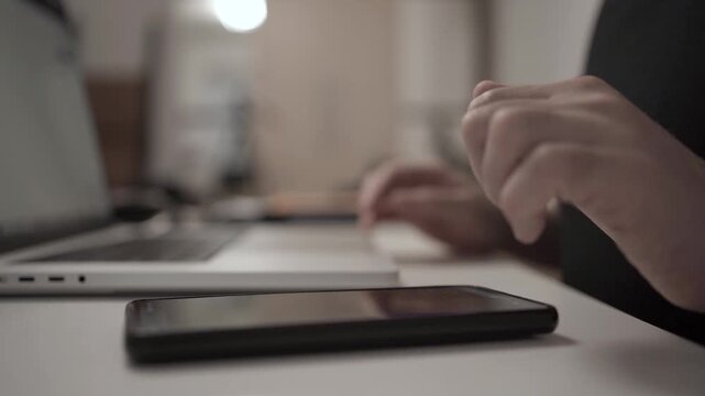 Multitasking Man Browsing Smartphone While Working on Laptop