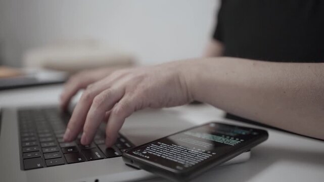 Multitasking Man Browsing Smartphone While Working on Laptop