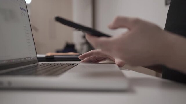 Multitasking Man Browsing Smartphone While Working on Laptop