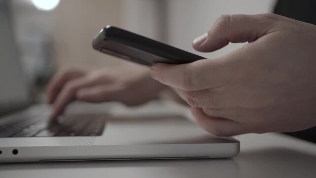 Multitasking Man Browsing Smartphone While Working on Laptop
