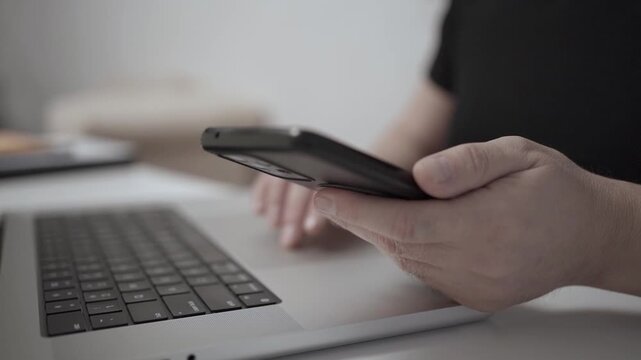 Multitasking Man Browsing Smartphone While Working on Laptop