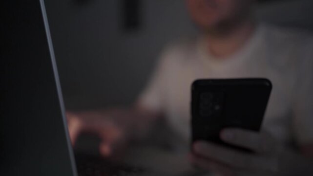Multitasking Man Browsing Smartphone While Working on Laptop
