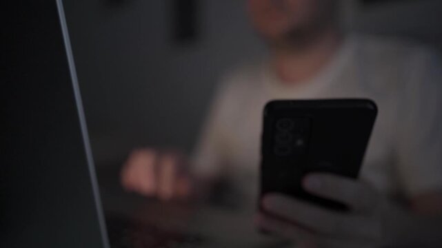 Multitasking Man Browsing Smartphone While Working on Laptop