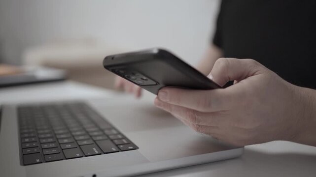 Multitasking Man Browsing Smartphone While Working on Laptop