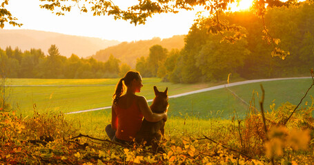 CLOSE UP: Young woman sitting in the sunlit meadow hugs her cute mixed breed dog while meditating...