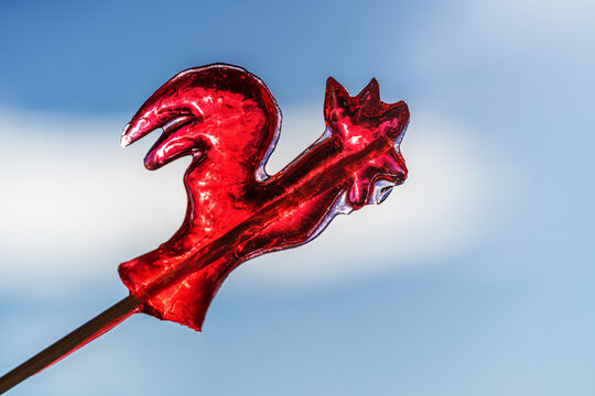 red rooster lollipop shines against blue sky and soft cloud in selective focus, playful minimal image for candy branding, childhood memories or bright summer concepts.