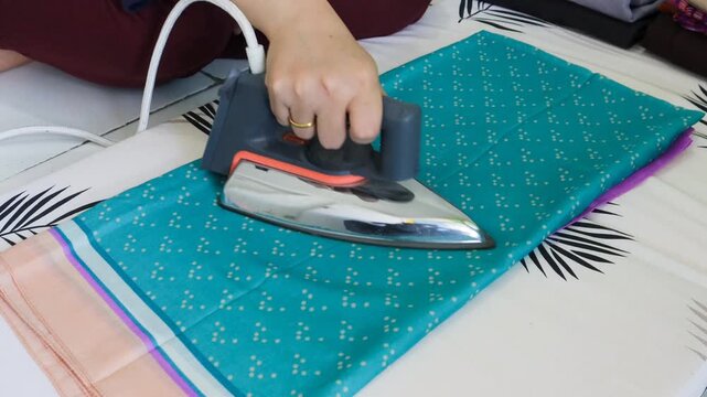 Close-up shot of an Asian woman ironing a garment at home, symbolizing cleanliness, everyday routine, and household. 