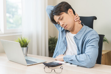 Body muscles stiff problem, ache asian young man pain neck and shoulder while sitting work on chair at home, male holding massaging rubbing, hurt or sore body. Healthcare people, office syndrome.