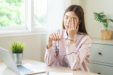 Eye problem concept, fatigue asian young woman tired eyes, irritated rubbing eye dry relief vision pain after work on laptop computer, eye strain, hand holding glasses, suffer migraine, bad blurry.