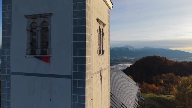 Bell tower of Church of Saint Primus and Felician in Jamnik with mountains view. Slovenia.