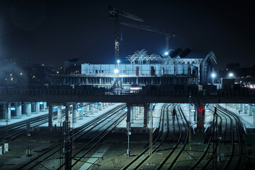 Nighttime view of railway construction site with multiple train tracks, overhead structures and artificial lighting highlights infrastructure work in city environment