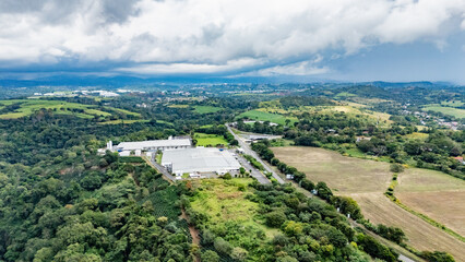 Aerial View of Industrial Warehouse Complex Surrounded by Green Fields and Tropical Forest