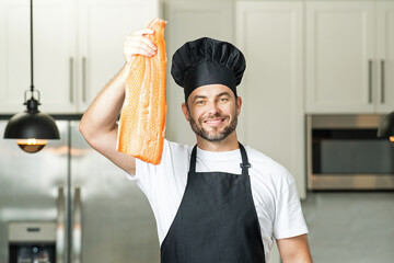 Chef in uniform cooking raw fish salmon fillet in the kitchen. Restaurant menu concept. Male chef in working uniform, black apron, chef hat. Fish salmon concept.