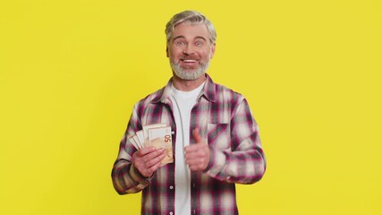 Mature man slowly counts money cash euro banknotes, showing evident delight and achievement from new funds. Middle-aged guy on yellow background exudes pride in successful financial outcome and growth