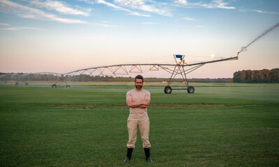 A farmer is watering irrigation farm. The Farmer on irrigation to water field. Farmer near Irrigation sprinkles water on grass. Irrigation system in action on the farm. Sprayer for watering field.
