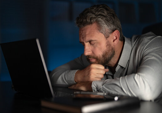 Tired businessman working late at night on laptop in night office. Overworked manager with headache. Stressed employee with anxiety while deadline. Freelancer career problems. Office worker late. - Powered by Adobe