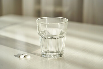 Glass of water with pills on table in sunlight symbolizing daily medication hydration and health routine.