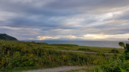 Evening coastal view on the Kuril Islands. Rolling green hills meet the sea under a dramatic sky....