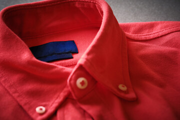 Close-up view of red button-down shirt focusing on collar and buttons. Fabric texture, stitching details of classic casual menswear style