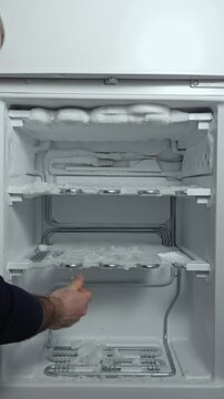Man defrosting freezer by removing ice buildup with hands, showing gradual progress in clearing shelves and improving appliance functionality