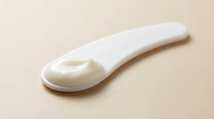 Beauty spatula with cream dollop on soft beige background  
