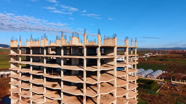 Distancing from a multi-storied frame of the building under construction. Metal rebars stick out from the concrete columns.