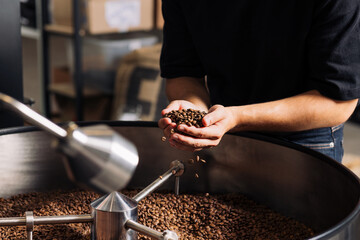 Unrecognizable barista holding fresh-roasting beans from a machine drum
