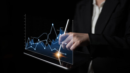 Business professional uses a tablet to analyze digital data trends and future projections in a dark...