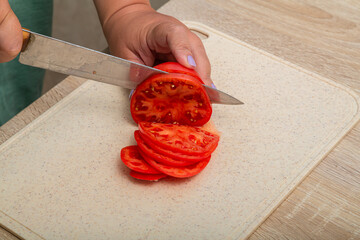 Red tomatoes are cut with a knife on a wooden board on the table