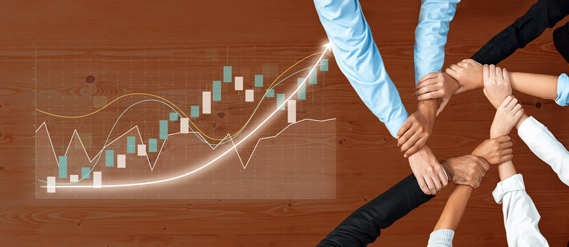 A diverse group of hands joins together over a financial chart on a desk, symbolizing teamwork and collaboration for business growth and success. Axiom - Powered by Adobe