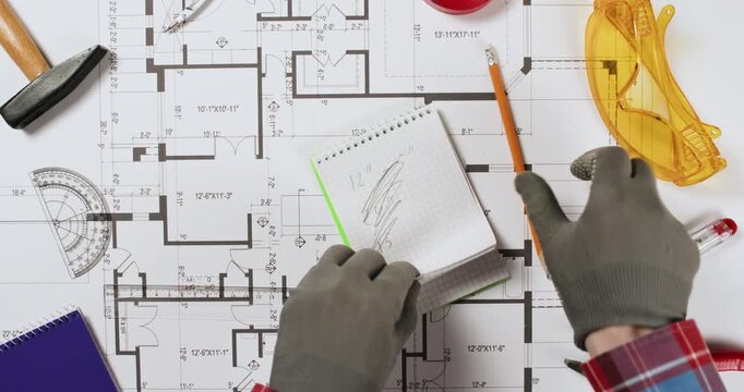 The worker takes measurements with a ruler on a paper plan of the house and writes the values ​​in a notebook, crosses out the values ​​in the notebook and tears out the sheet, destroying it.