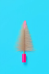 Minimalist holiday beauty concept featuring a mascara brush stylized as a Christmas tree on a turquoise background.