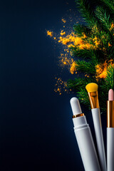Festive flat lay featuring makeup tools, cosmetic bottles, pine branches, and spices on a dark background. Holiday beauty and skincare concept.