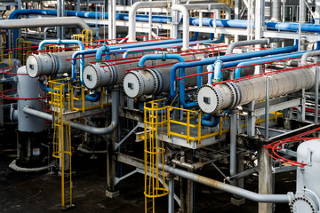 Series of pipes are connected to a large tank. The pipes are blue and red. The tank is large and is surrounded by a yellow railing