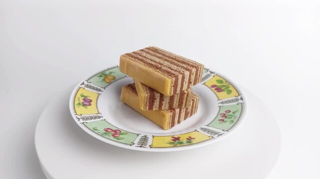 Stacked traditional Indonesian lapis legit layered cake on rotating plate. Sweet spicy dessert on white background.

