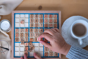 female hands placing number into Sudoku puzzle, solving puzzle on wooden board, Brain exercise, cognitive health, mental agility in mature age